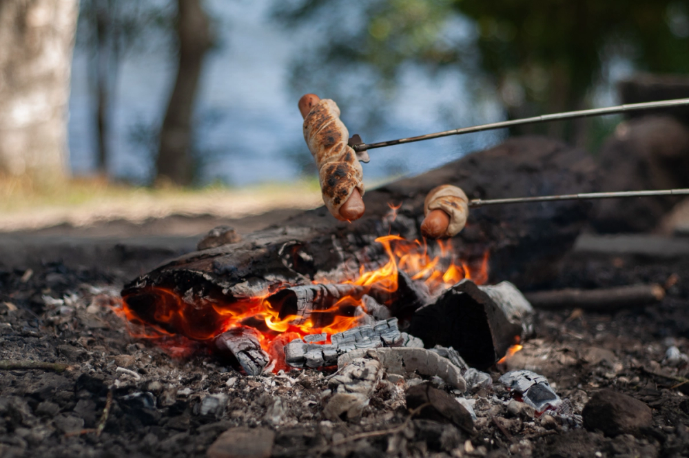 Grillpølser surret i deig grilles over et lite, glødende bål i naturen.