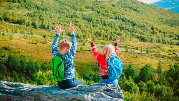 En jente og en gutt på en stein i fjellet med tursekk på ryggen.