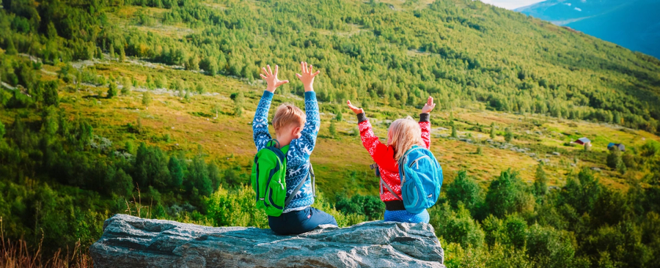 En jente og en gutt på en stein i fjellet med tursekk på ryggen.