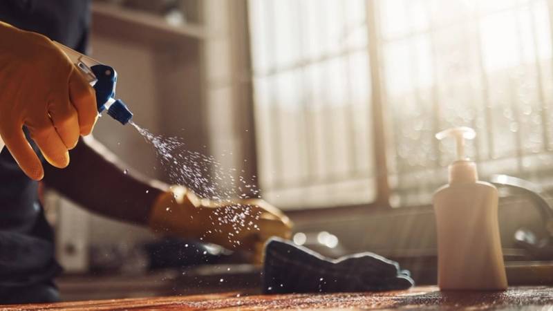 Hånd som sprayer kjøkkenbenk med vaskemiddel for å vaske kjøkkenbenken.