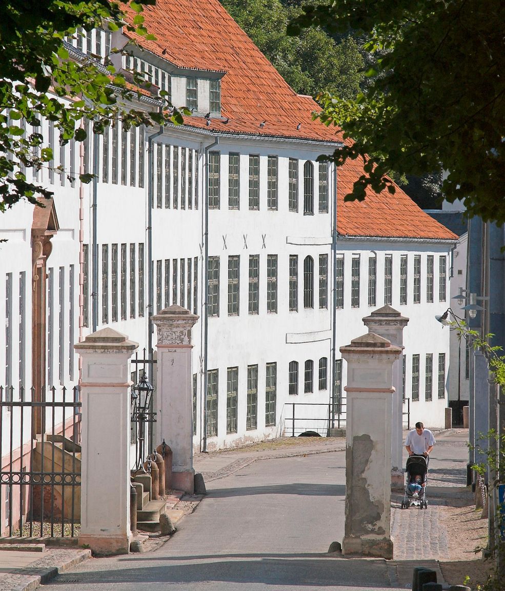 Hvid fabriksbygning med rødt tegltag ved indkørslen til Brede Værk set fra vejen gennem den gamle portåbning