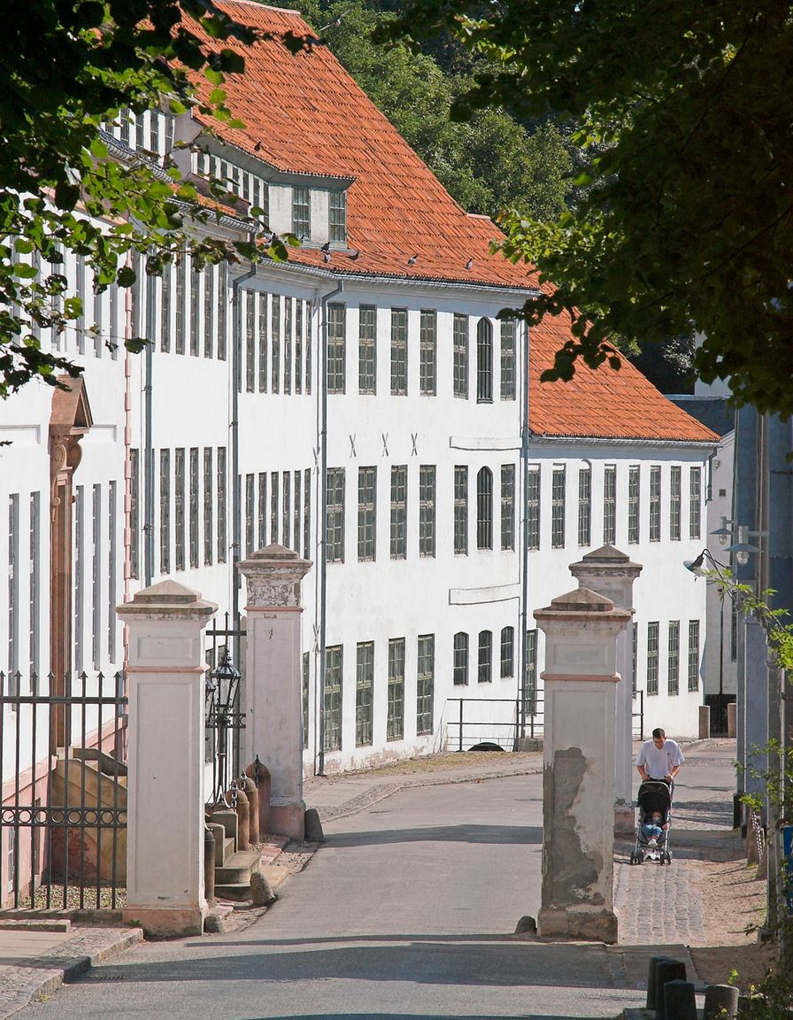 Hvid fabriksbygning med rødt tegltag ved indkørslen til Brede Værk set fra vejen gennem den gamle portåbning