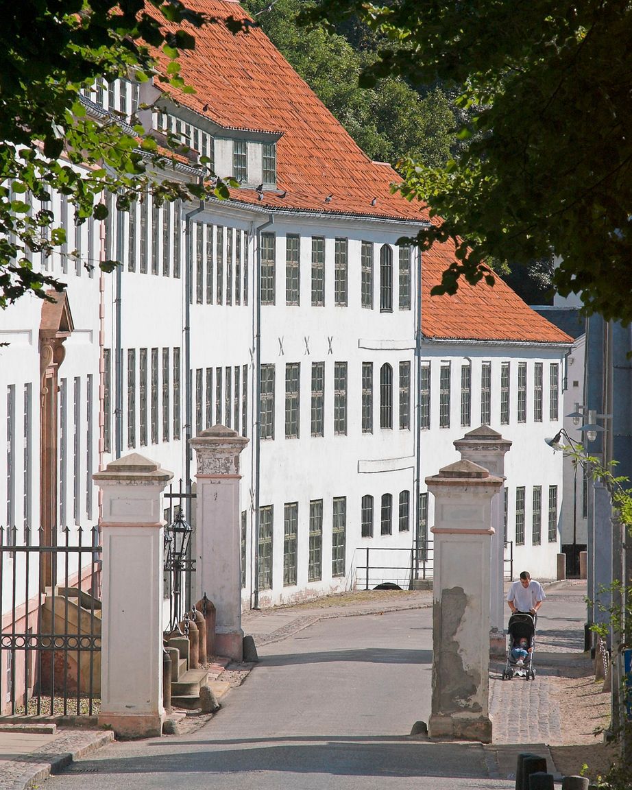 Hvid fabriksbygning med rødt tegltag ved indkørslen til Brede Værk set fra vejen gennem den gamle portåbning