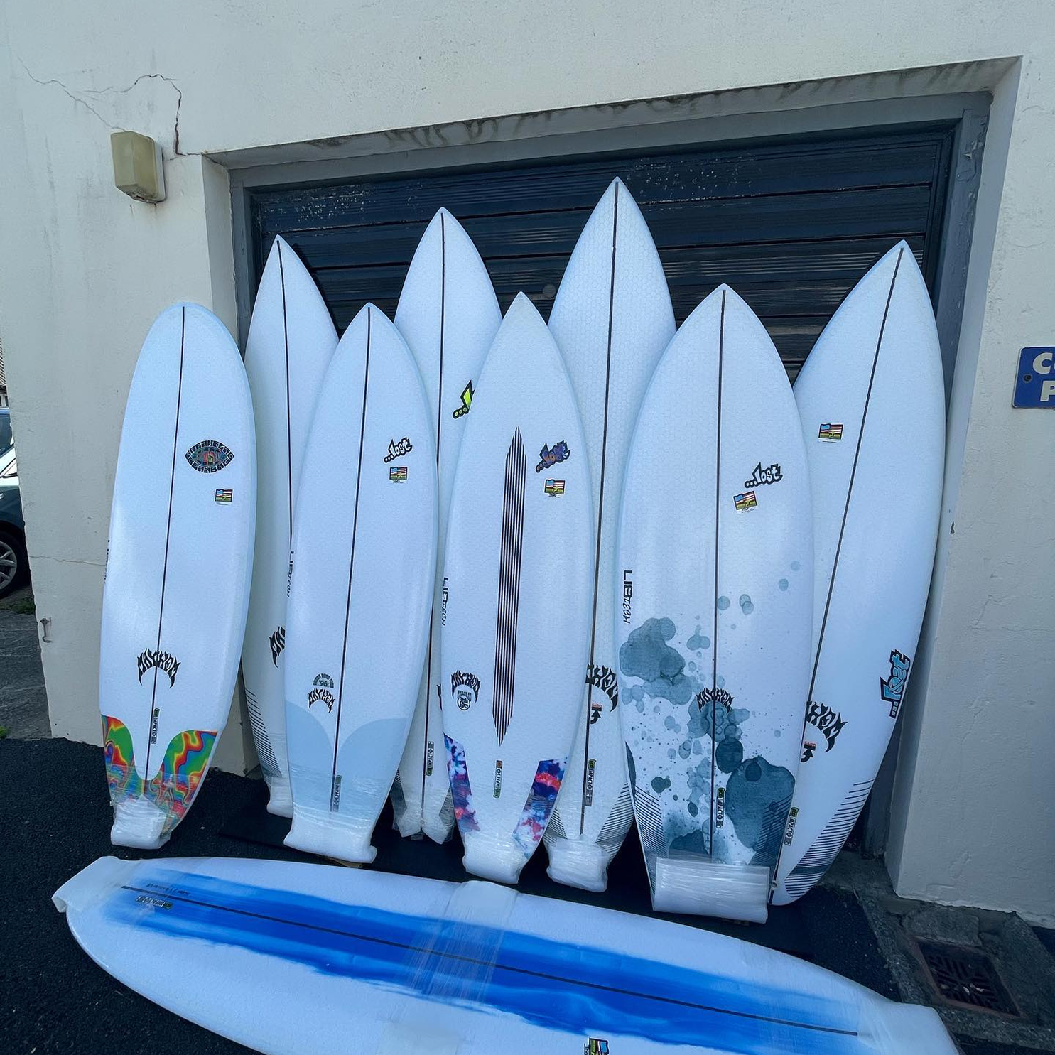 Multiple white surfboards stood up against the wall outside
