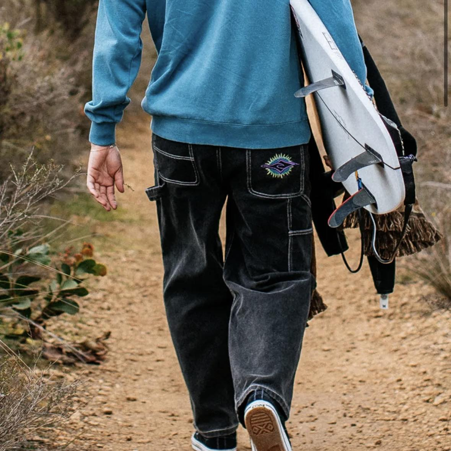Man holding surfboard from waist up walking from behind