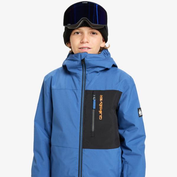 Young boy with goggles and a blue and black quicksilver coat