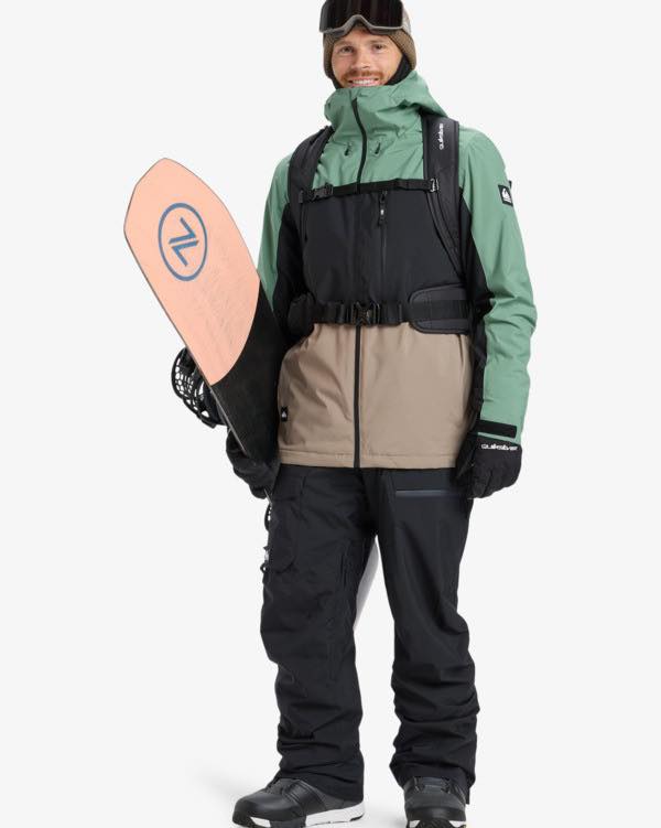 Man smiling in green coat with snowboard