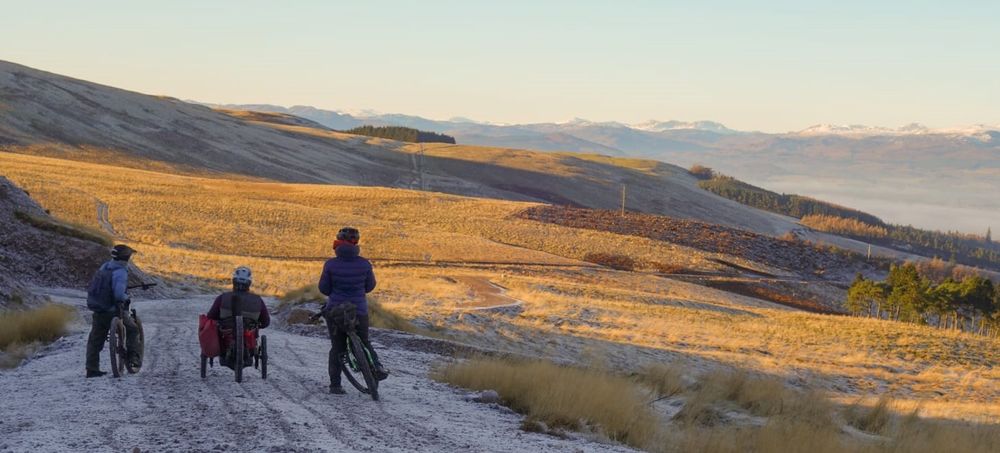 photo of an adaptive rider and two two wheel riders enjoying far reaching views down the glen to the hills beyond