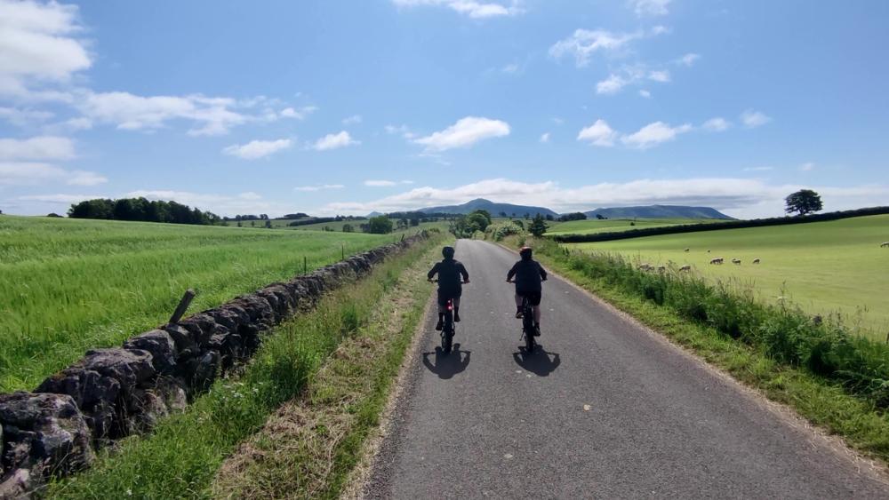 Two cyclists on a quiet road, with hills in the background