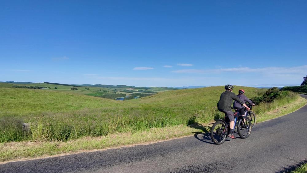 The view north over Glenfarg Reservoir to Strathearn Two cyclists on a quiet country road, with a view over fields