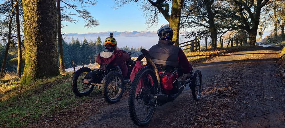 photo of two adaptive cyclists looking out on the views of the hills behind Crieff from the road