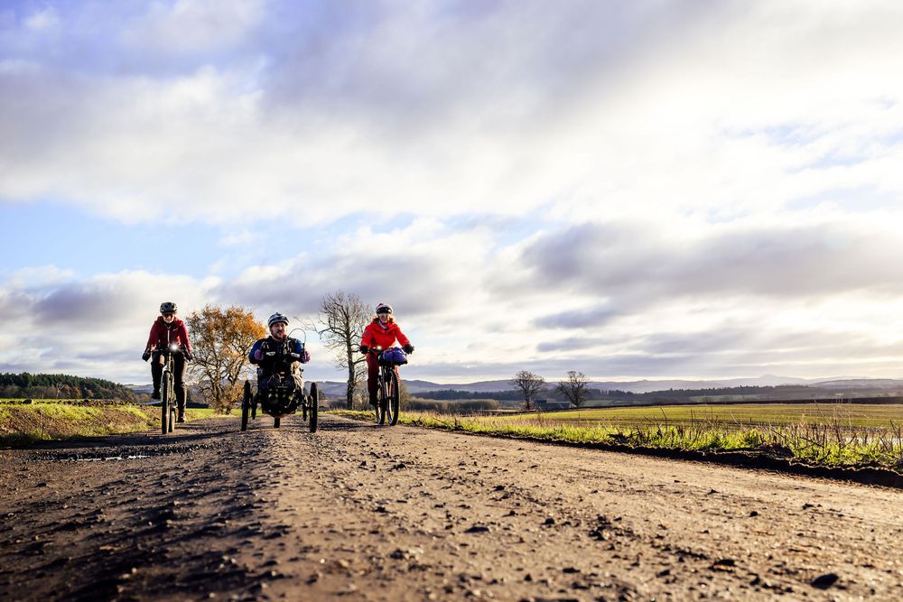 a photo showing an adpative rider and two two wheel cyclists on a gravel road