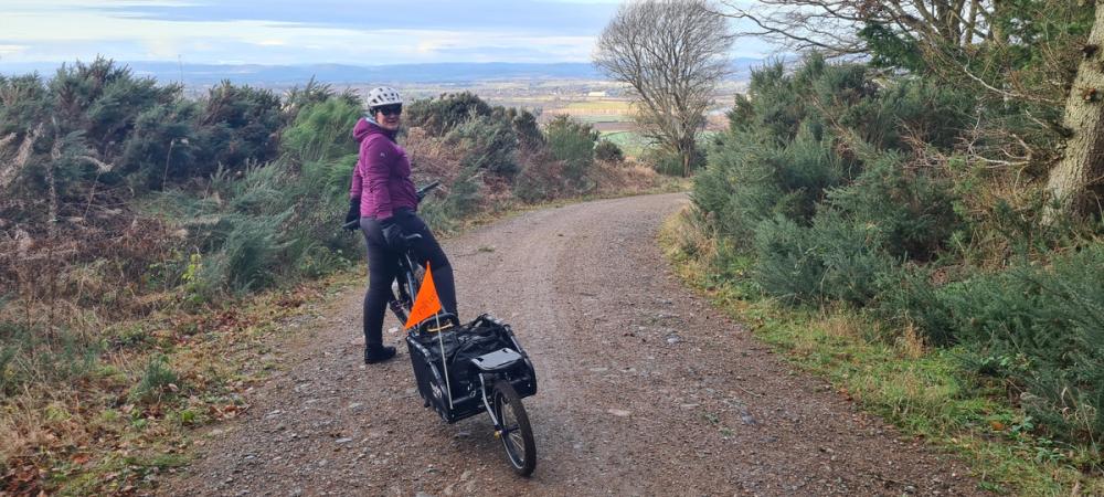 photo showing a cyclist towing a tailer riding on a gravel track with far reaching views into the Strathmore valley