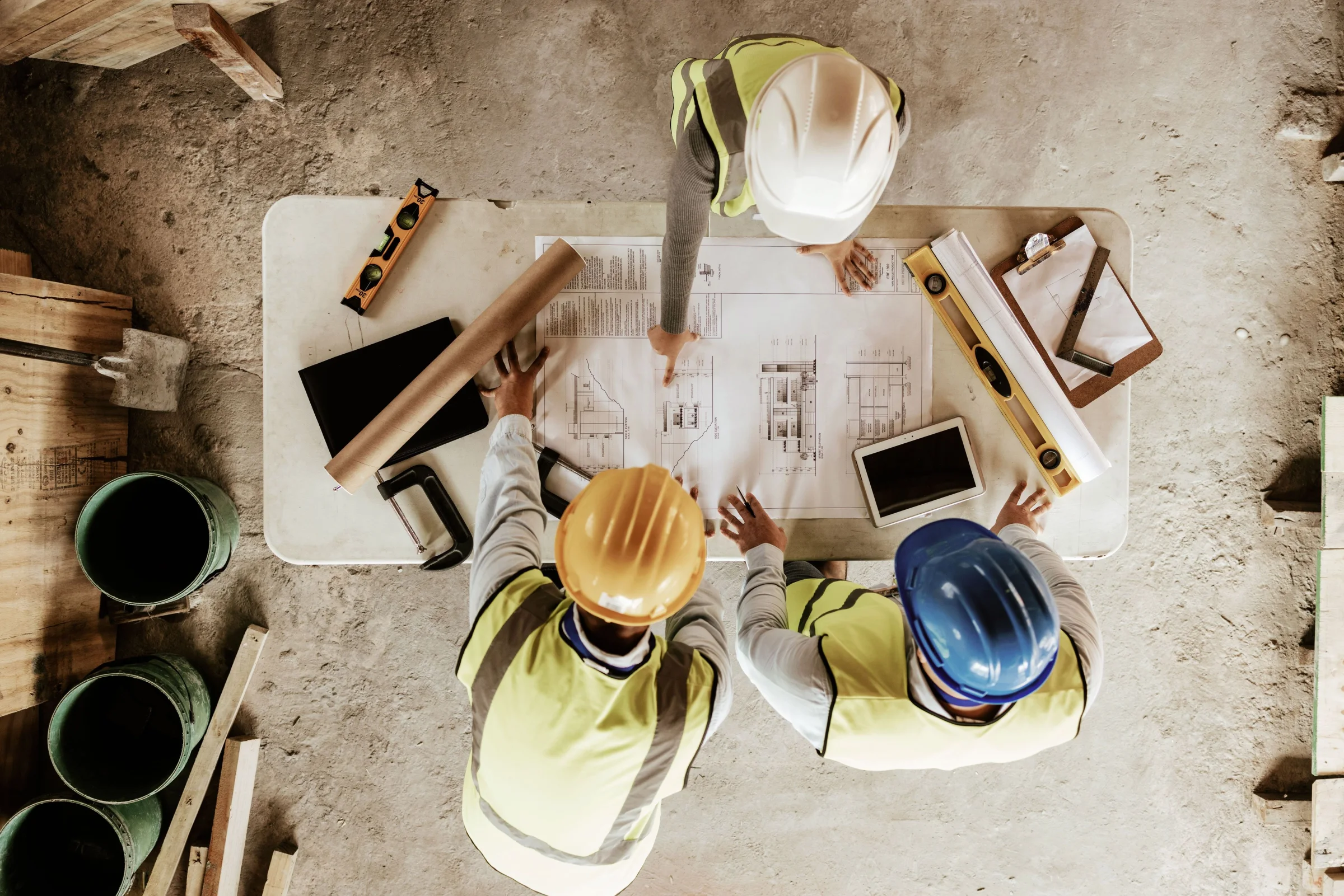construction workers in hardhats looking at plans around table