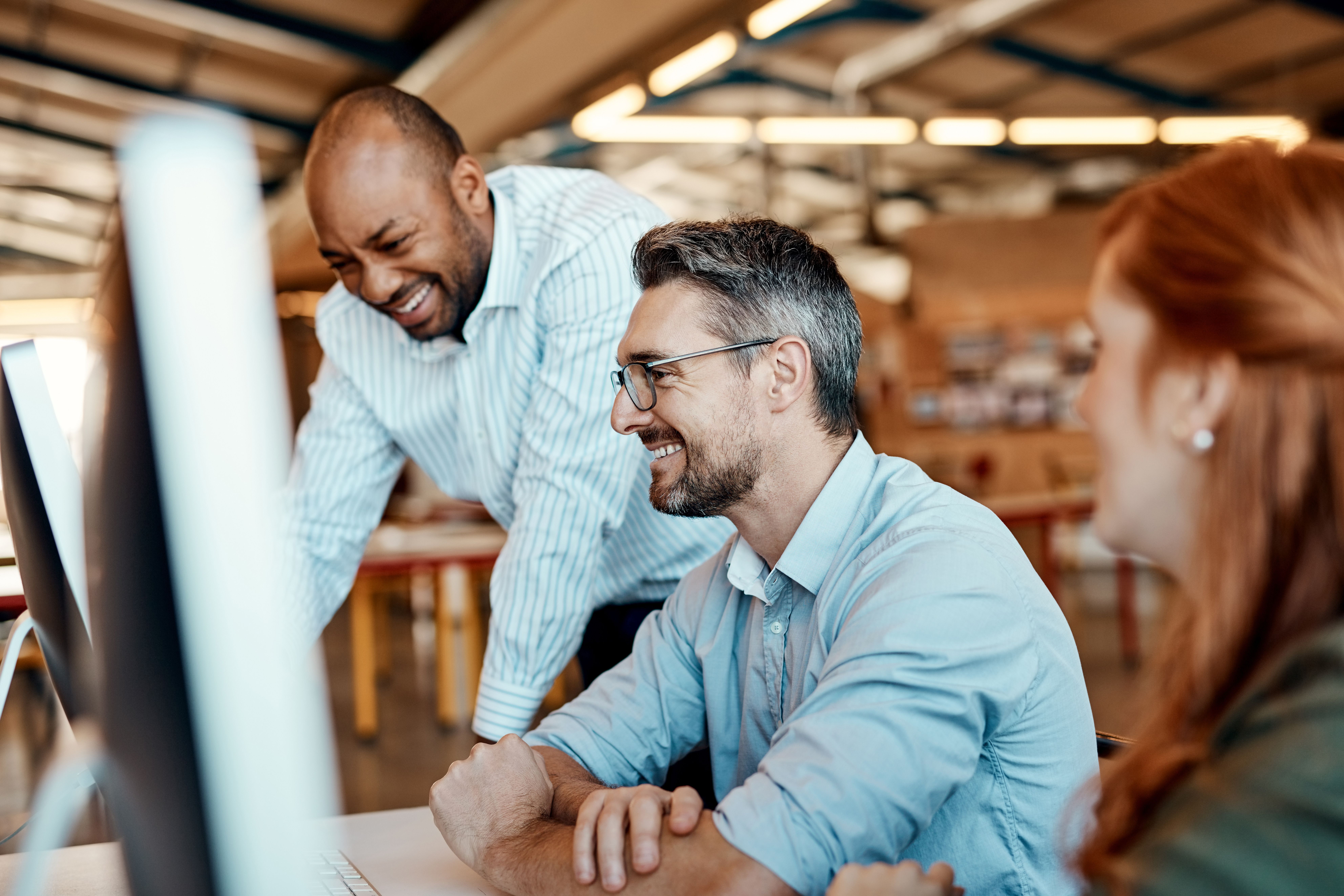 three colleagues at office computers laughing