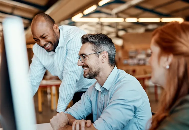 three colleagues at office computers laughing