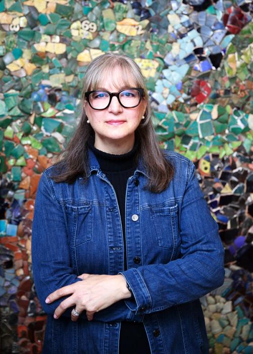 Mary Fibich standing in-front of a colorful background crossing her arms.
