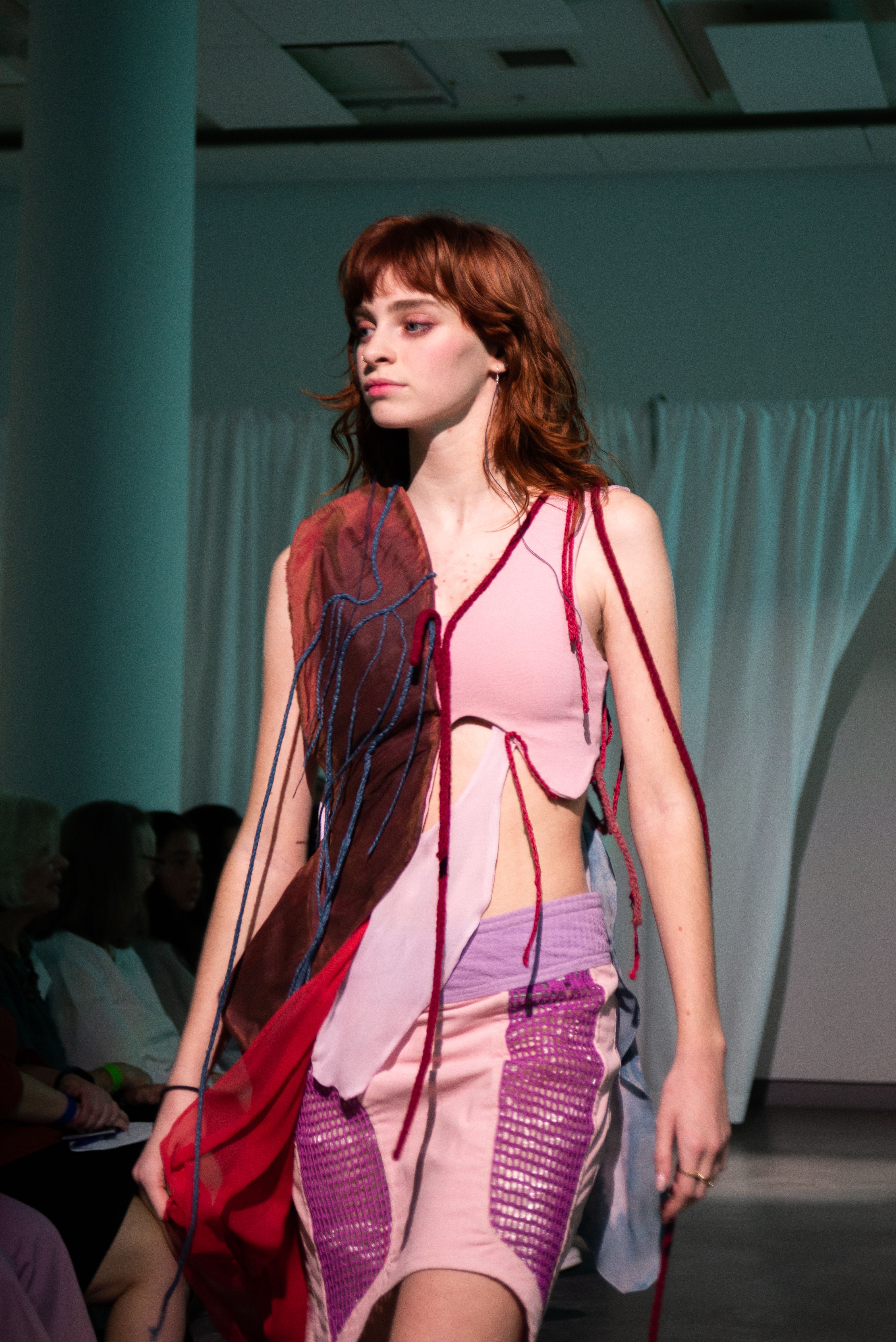 A model on the runway wearing an asymmetrical dress with dangling flesh-colored fabrics.