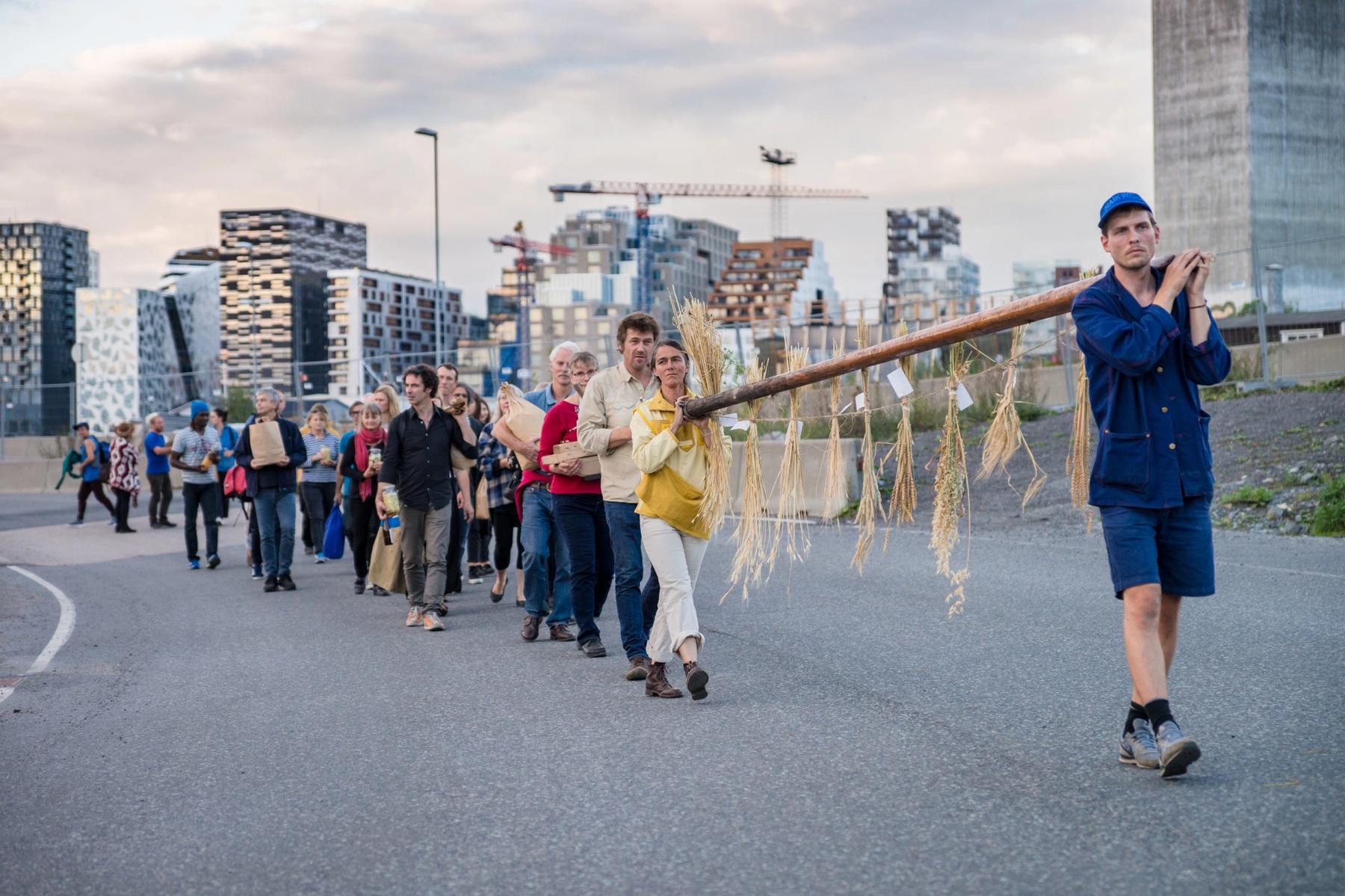 People marching in a city carrying a large branch with hanging bunches of dried plants.