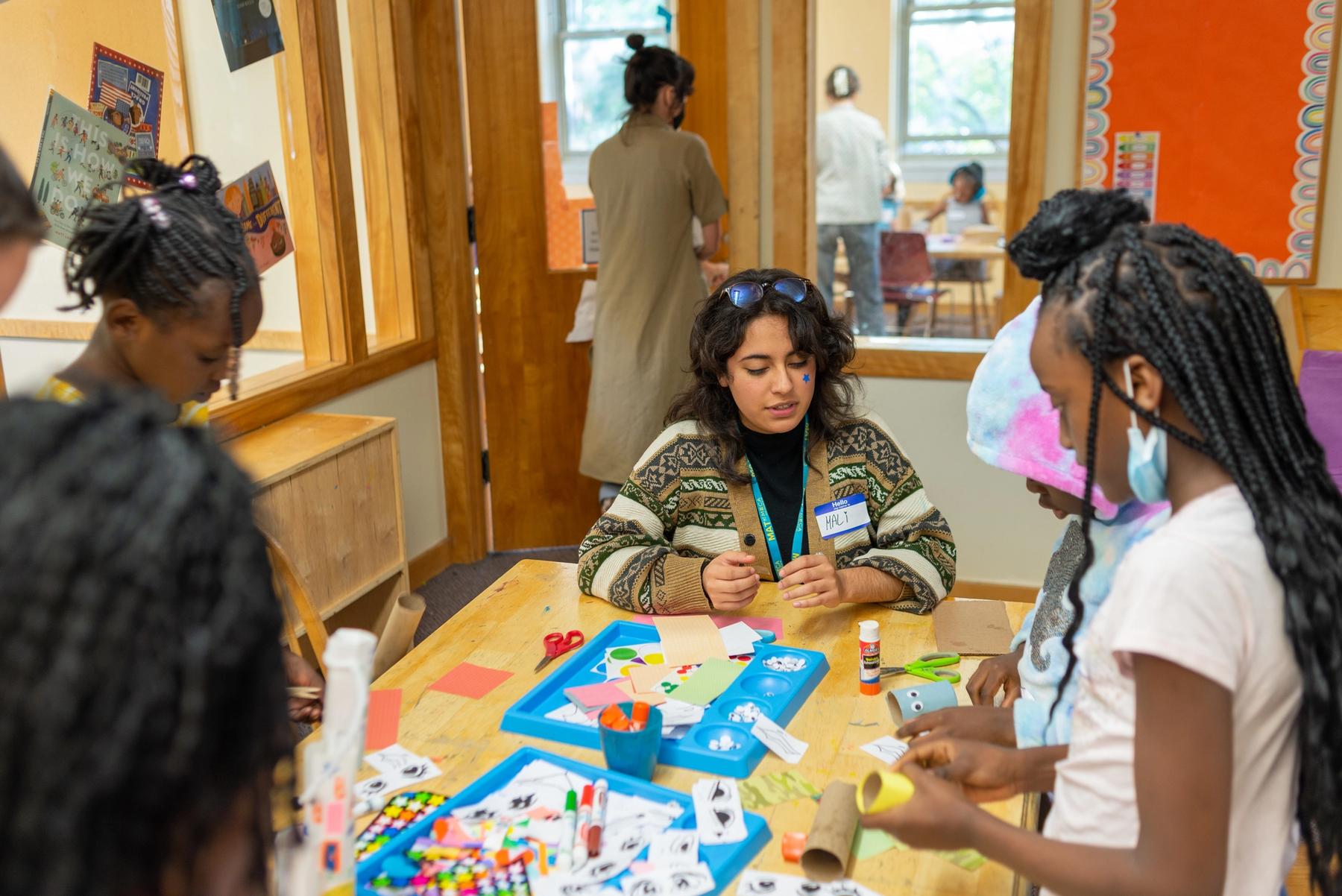 MAT student working with a group of children to make toilet paper roll art using stickers, collage, and markers.