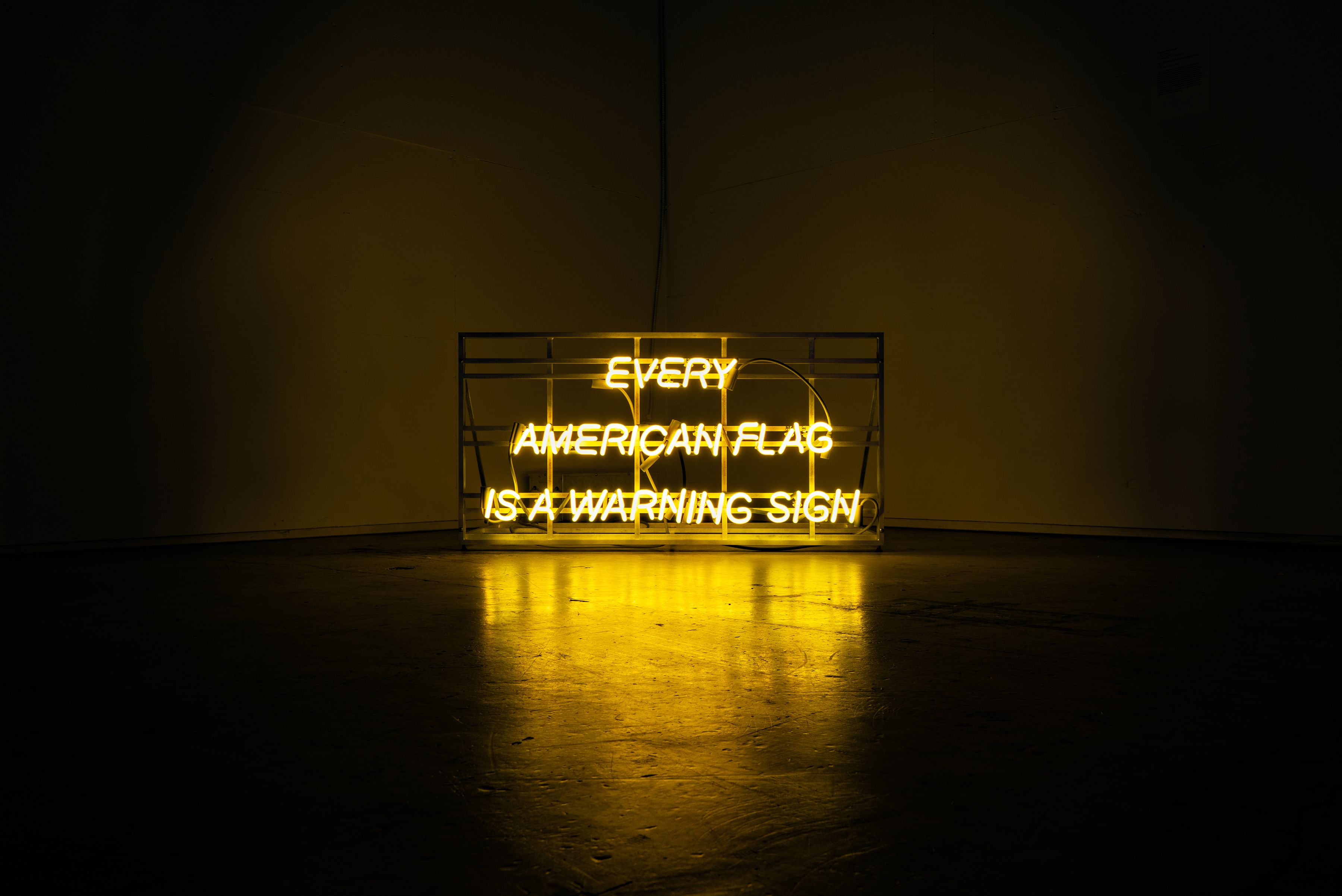 A yellow neon sign that reads, "EVERY AMERICAN FLAG IS A WARNING SIGN"