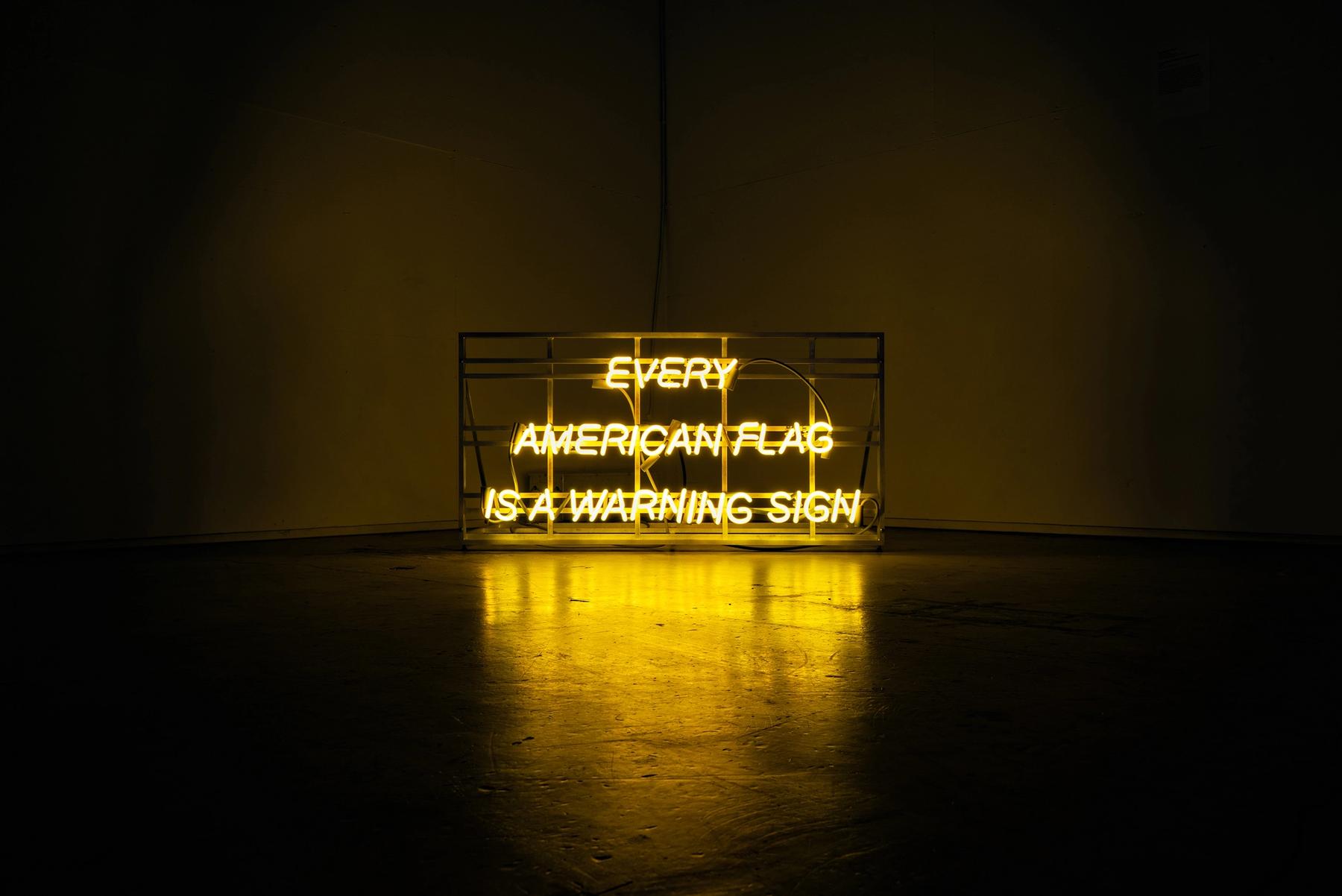 A yellow neon sign that reads, "EVERY AMERICAN FLAG IS A WARNING SIGN"