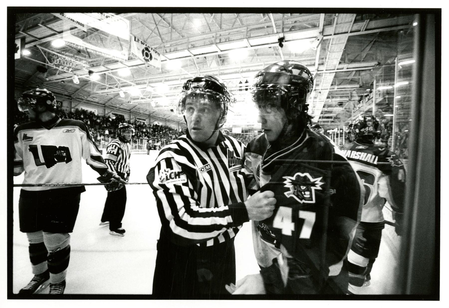 Black and white photograph of a hockey referee grabbing the lapel of a hockey player while looking away.