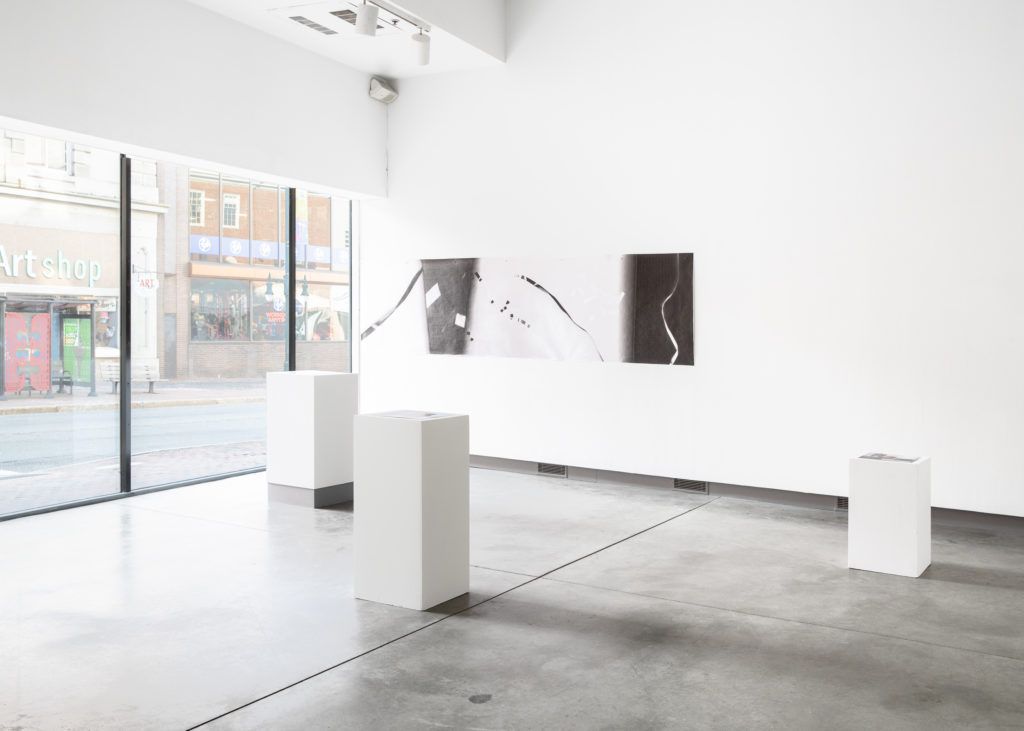 Gallery view of a large print and three white pedestals.