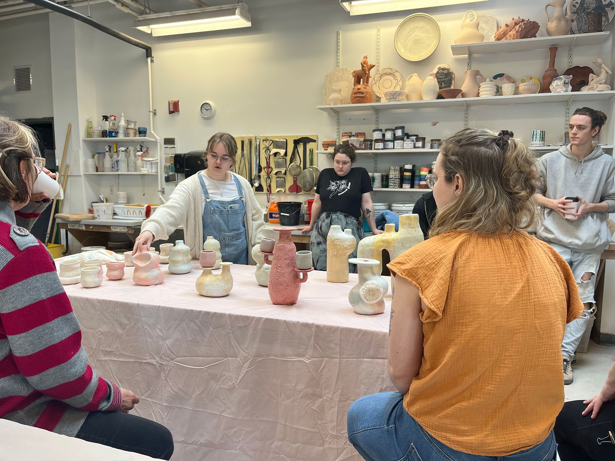 A student presenting a table full of ceramic vessels for a critique.