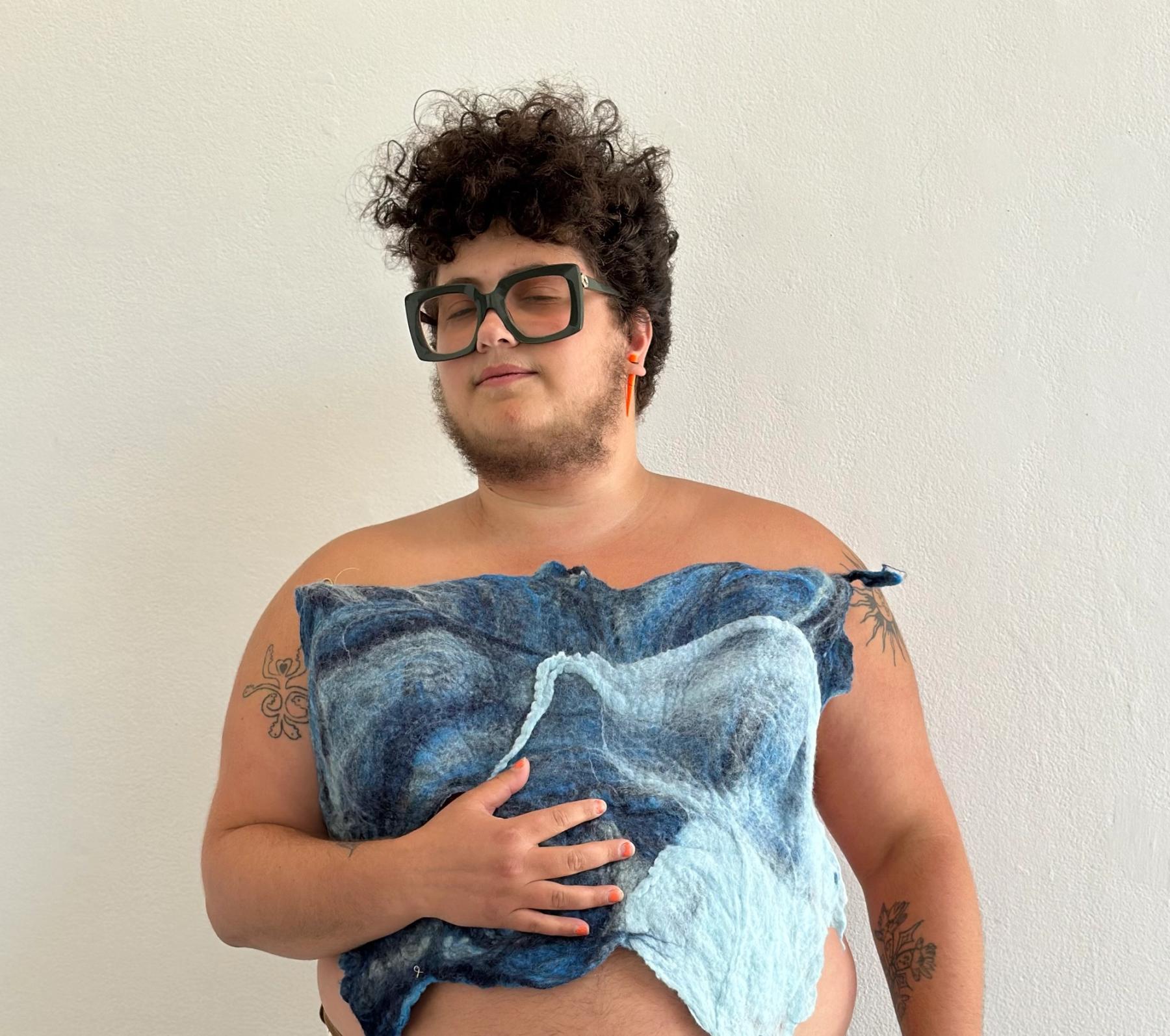 An artist holding a felted garment to his chest.