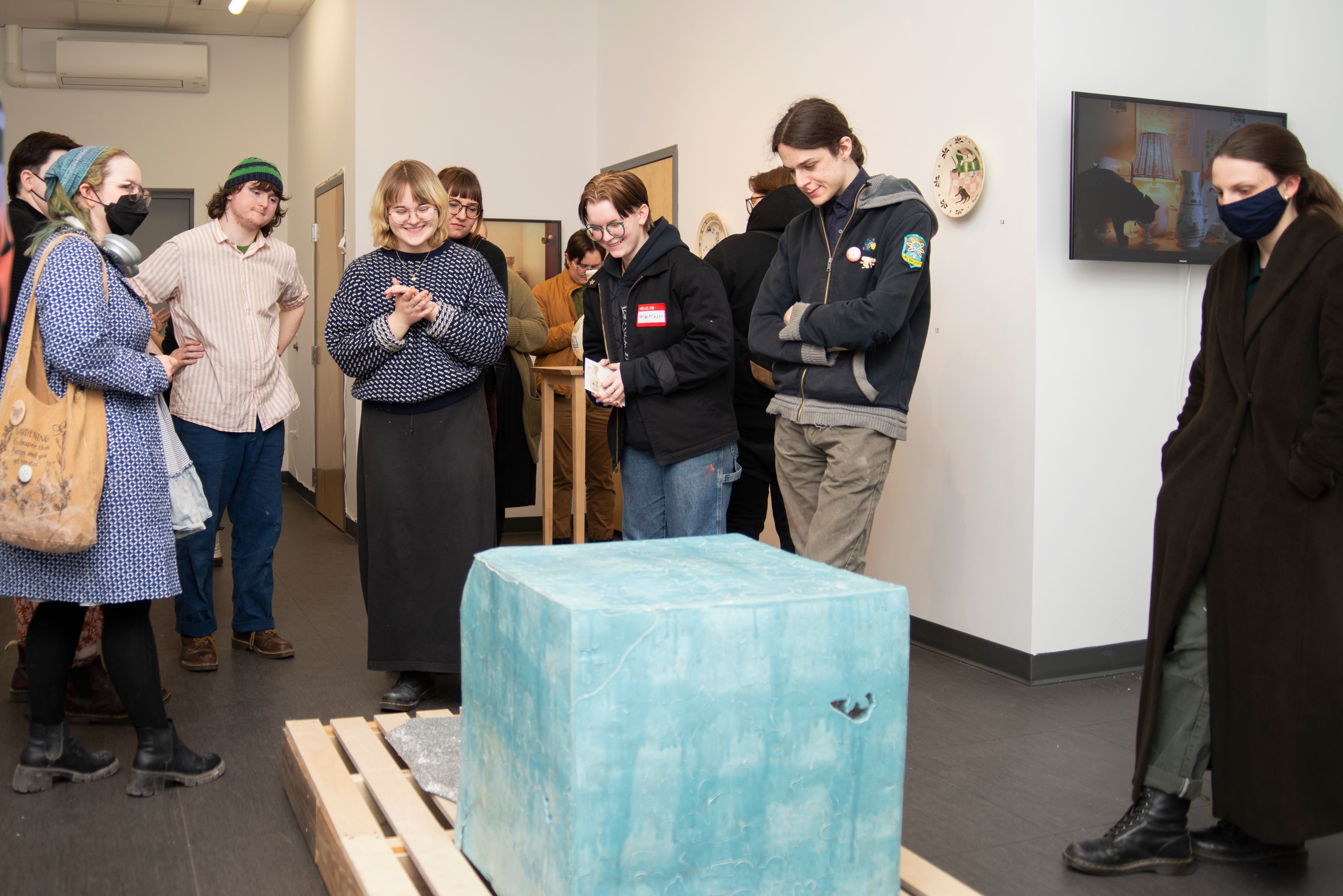 A crowd of people looking at a large blue ceramic cube in a gallery.