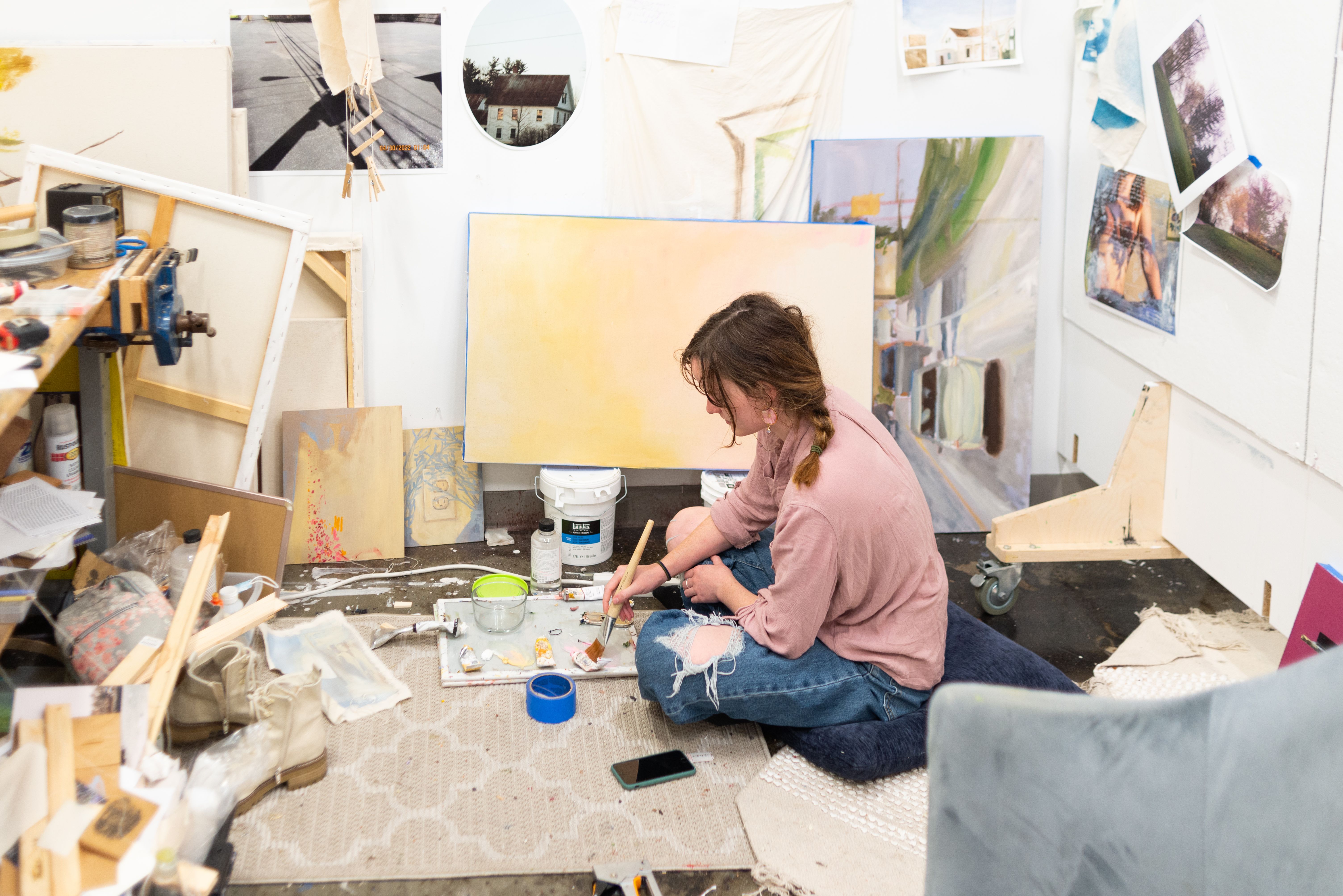 MFA Student painting on a canvas in a studio full of materials.