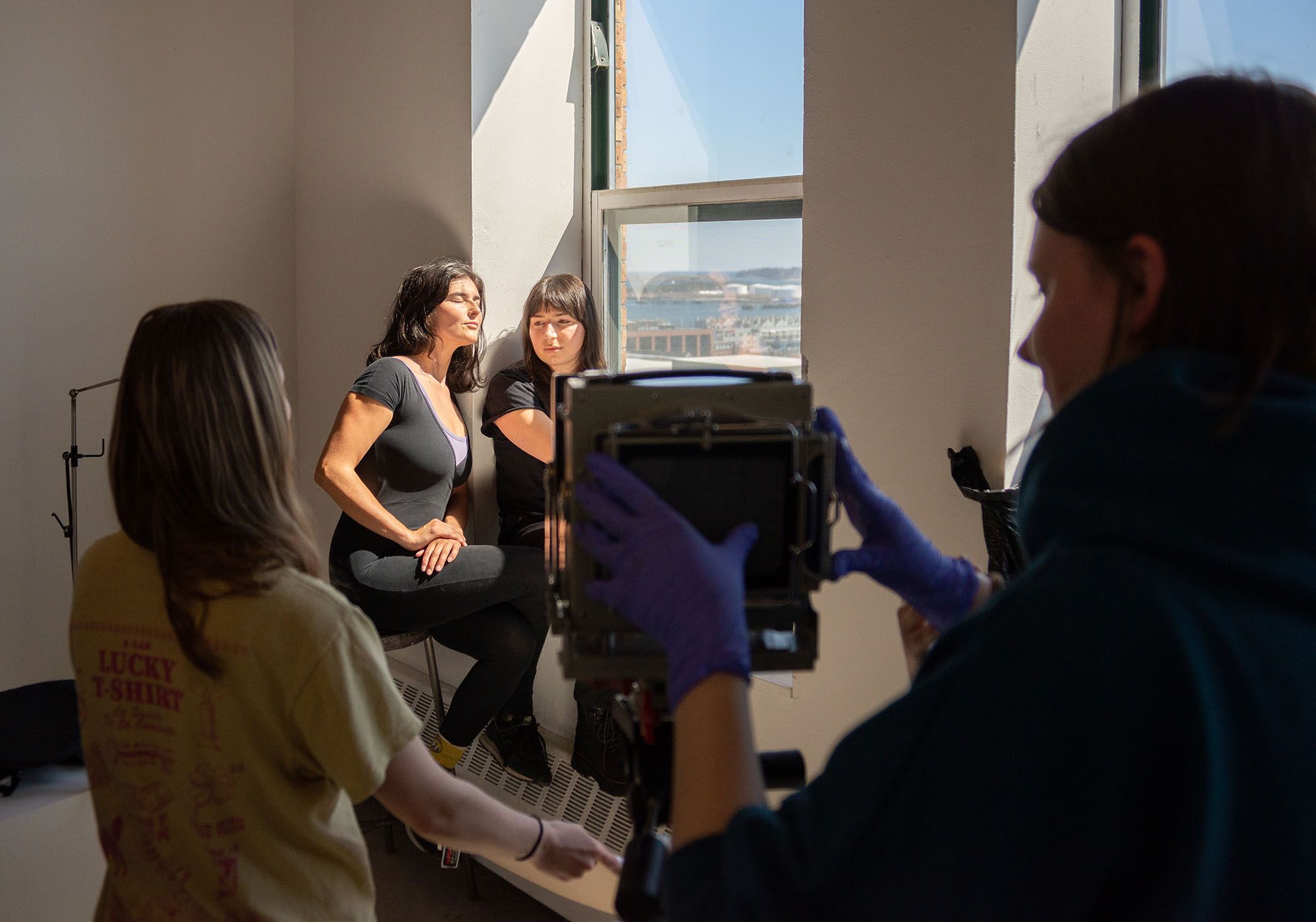 Students photographing two women sitting in a sunny window.