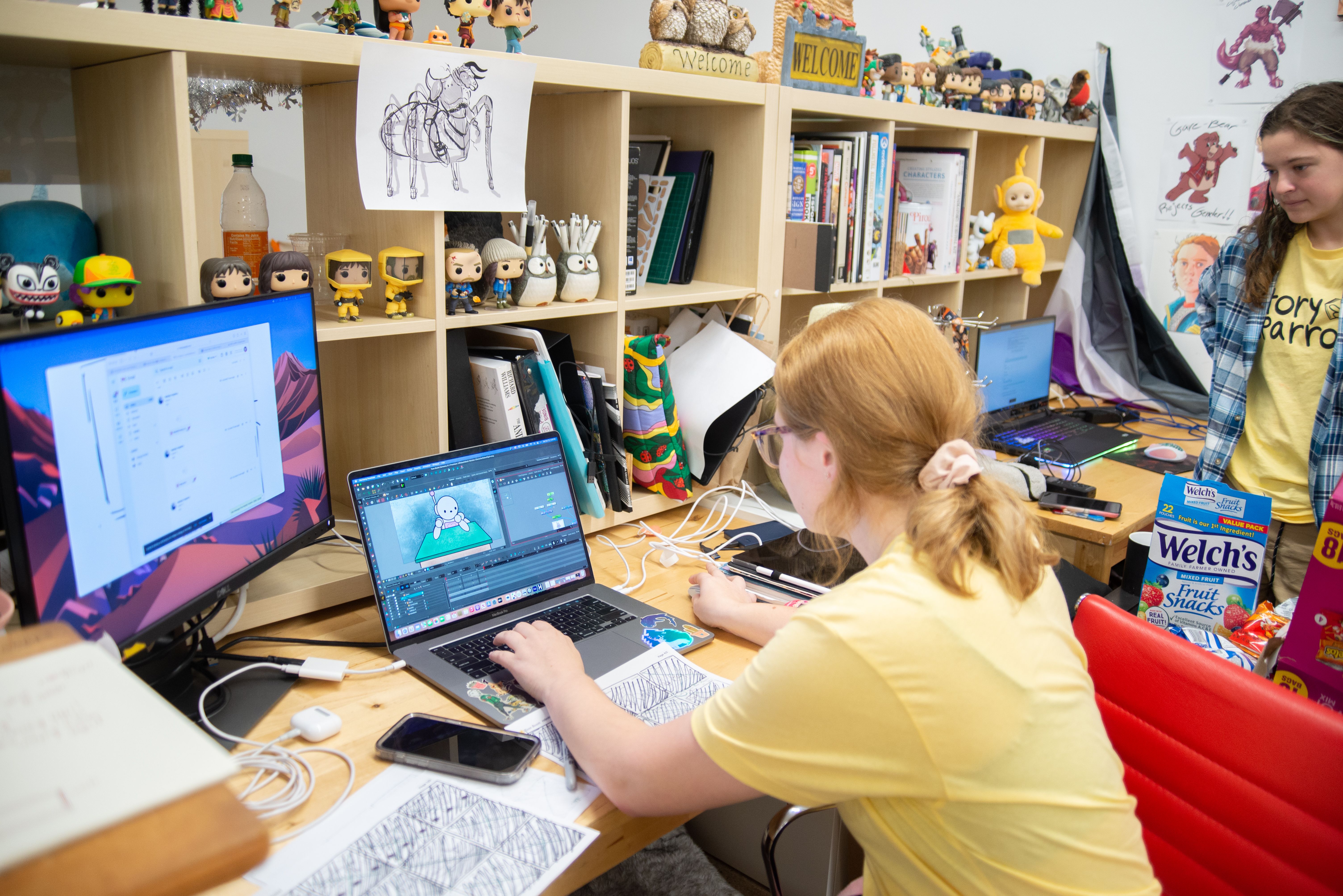 Student at their laptop working on an animation program with drawings scattered across their desk.