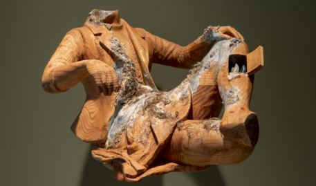 Floating wooden sculpture depicting a headless and footless figure seated wearing a suit jacket with an open door on their shin.