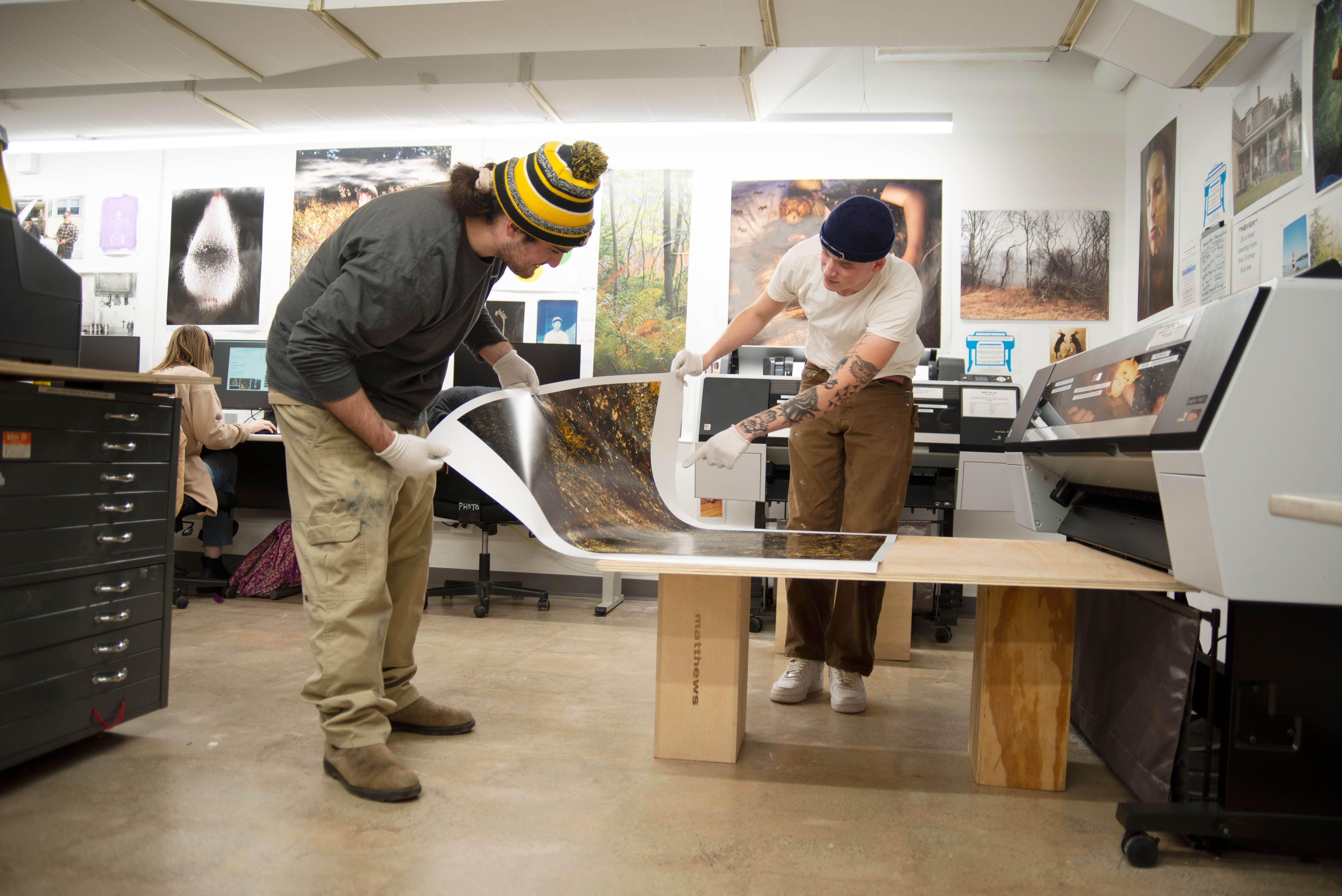 Two students checking a newly printed photograph in front of an inkjet printer.