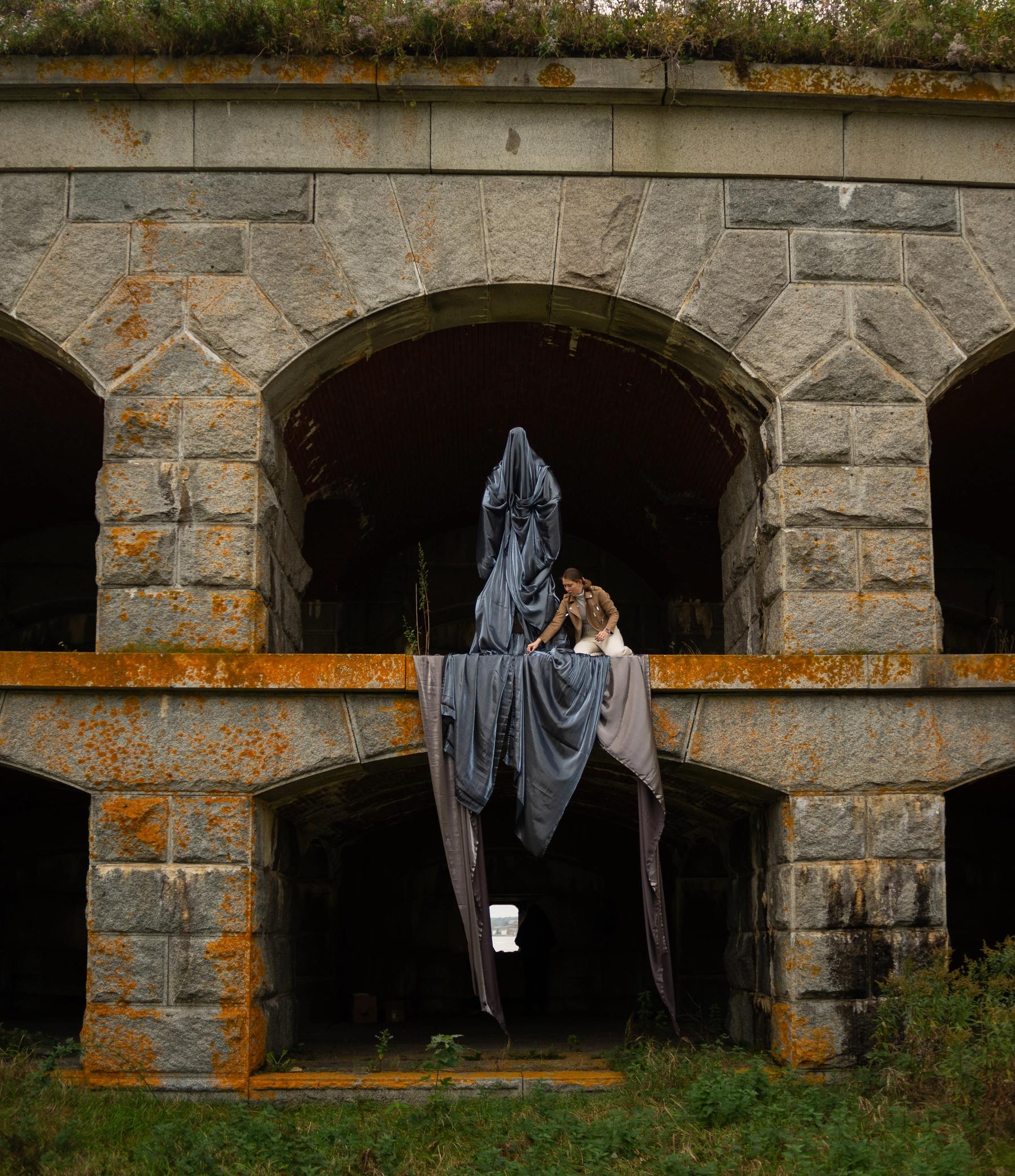 Student installing a sculpture of a figure draped in black fabric in an archway of Fort Gorges.