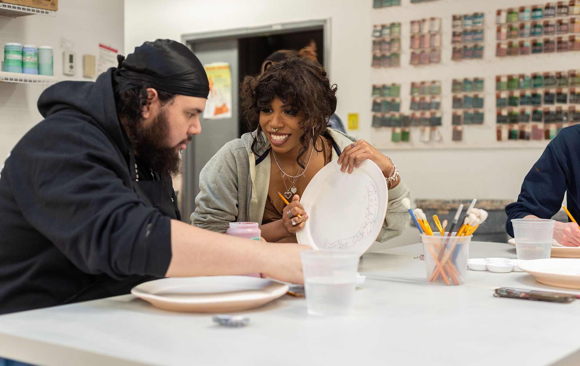 Two people smiling while painting ceramic plates.