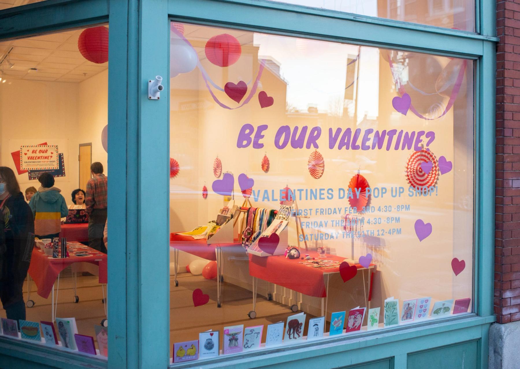 49 Oak front windows with vinyl reading "Be our Valentine?" looking into a pop-up shop full of Valentine's Day cards.