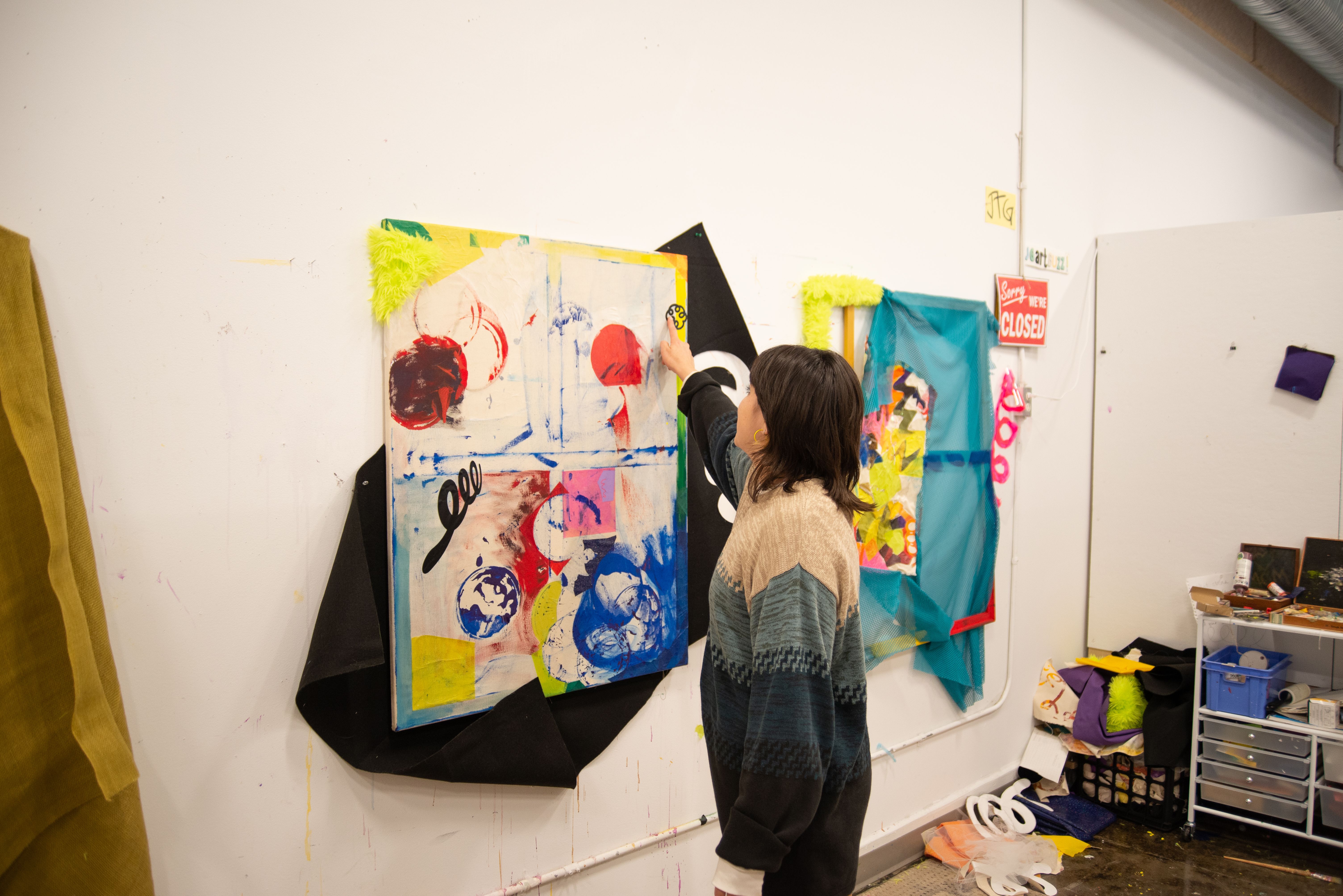 MFA studios with a student pointing towards one of their in-progress paintings.