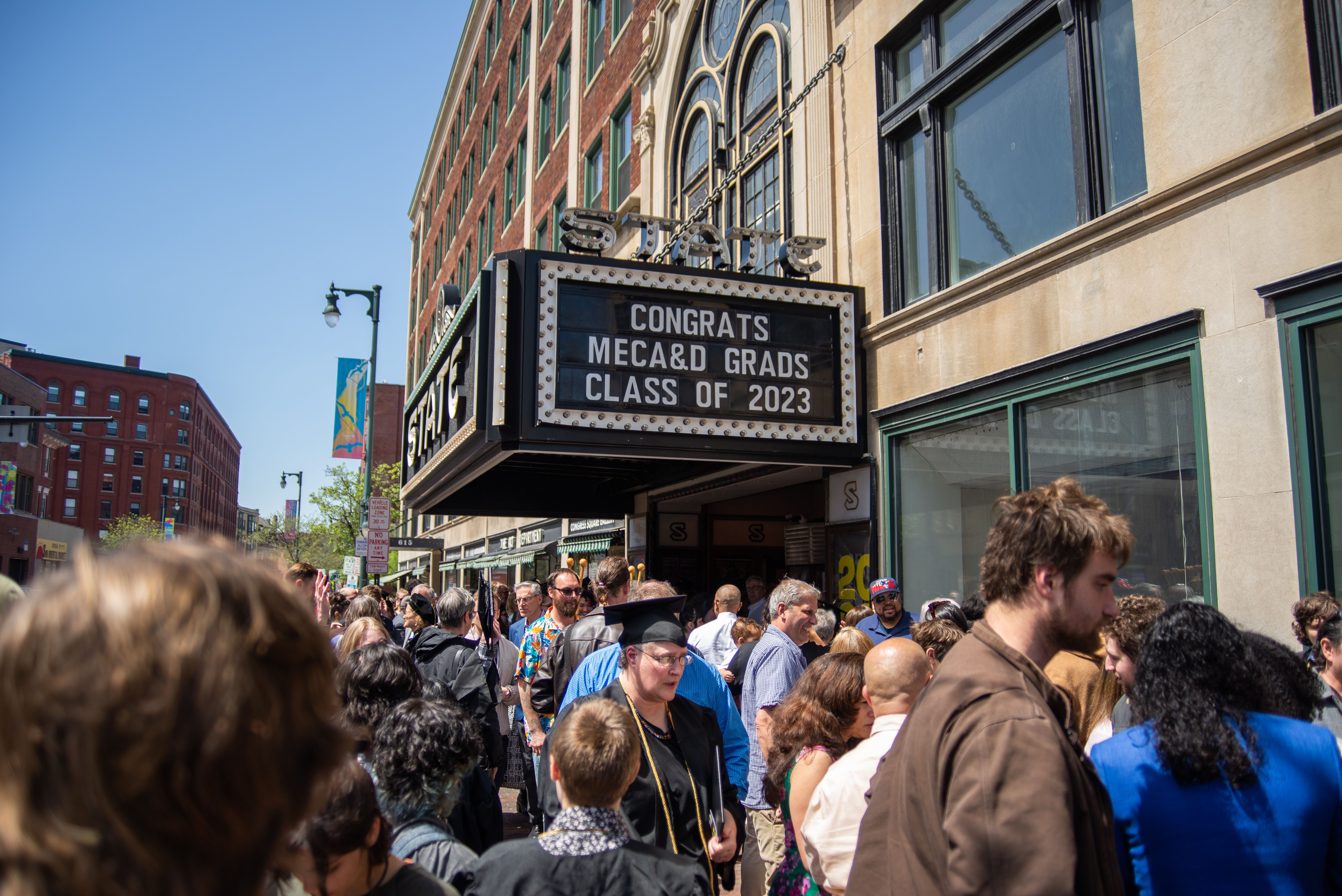 A crowd of people below the State Theater sign that reads "Congrats MECA&D Grads Class of 2023"