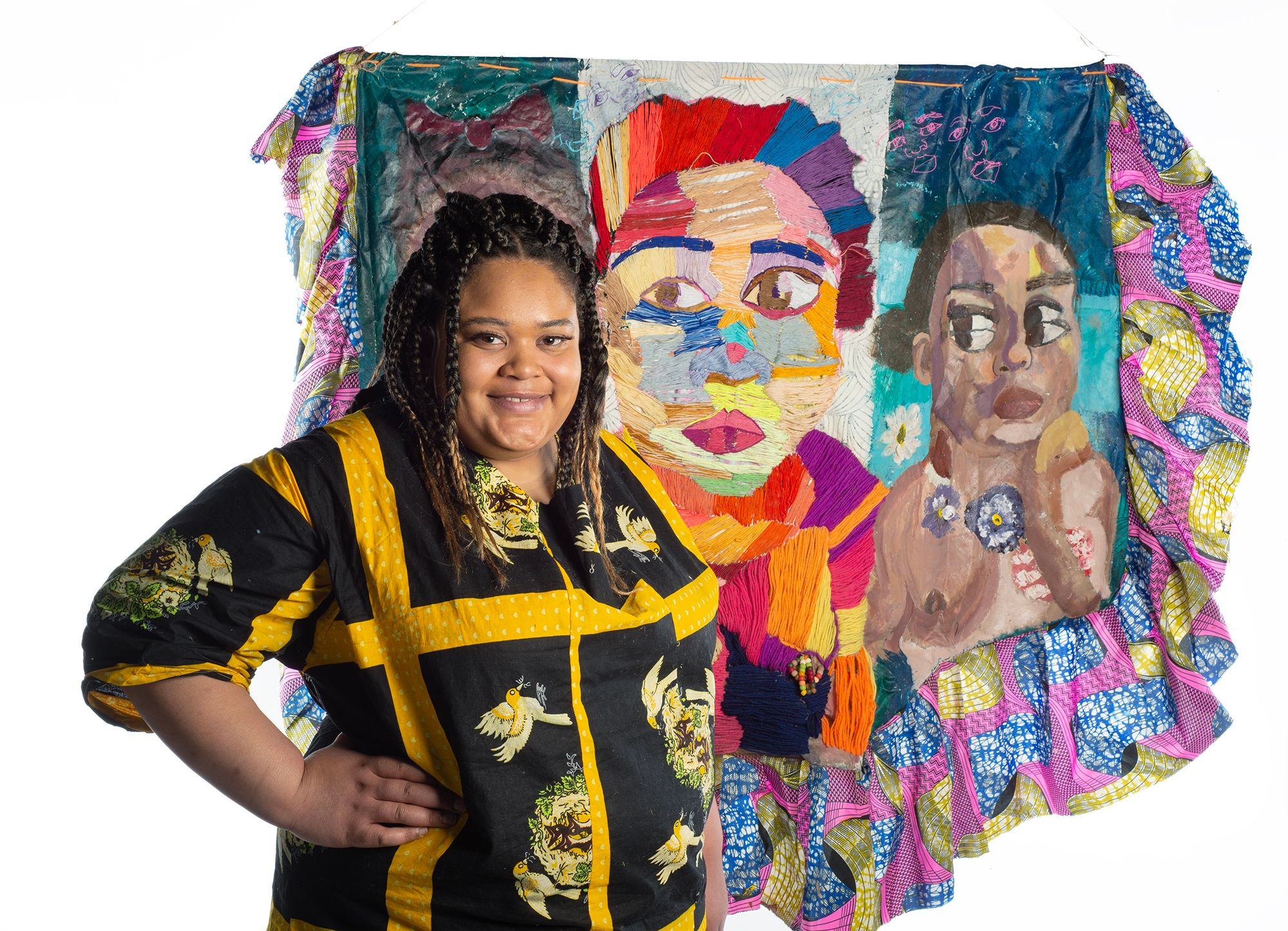 A student wearing a Nigerian dress, next to an installation of a painted quilt piece.