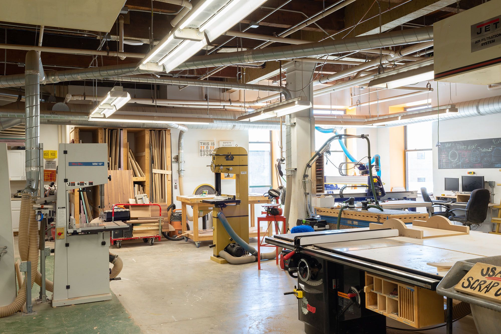 Woodworking & Furniture Design studio view with bandsaws, a table saw, and a chalkboard.