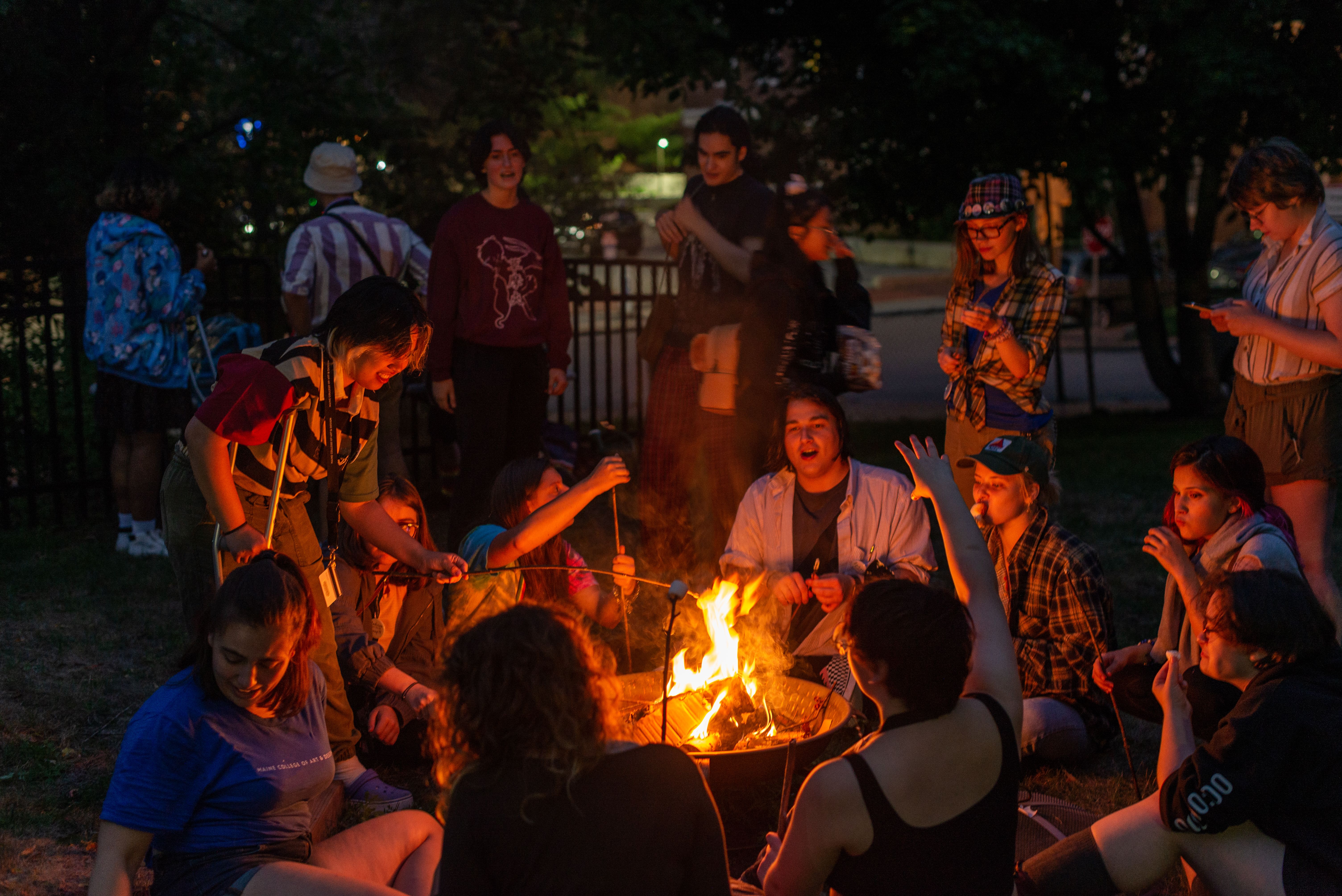 Students surrounding a bonfire, roasting marshmallows.