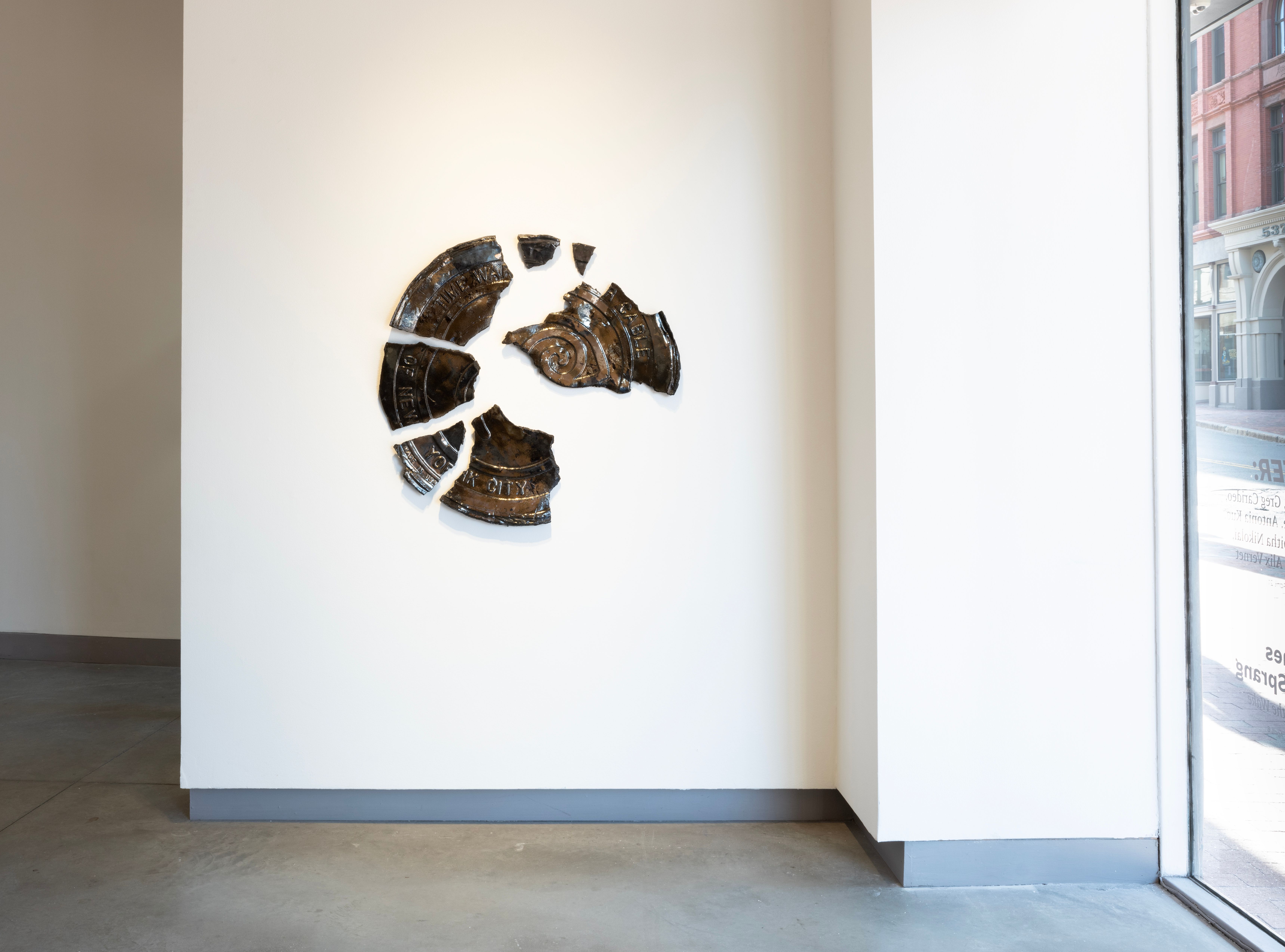 Installation view of a ceramic sculpture that resembles a brown broken circle.