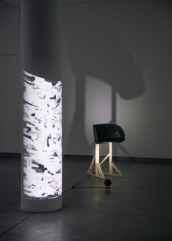 Gallery view of a distorted projection on a column next to a sculpture.