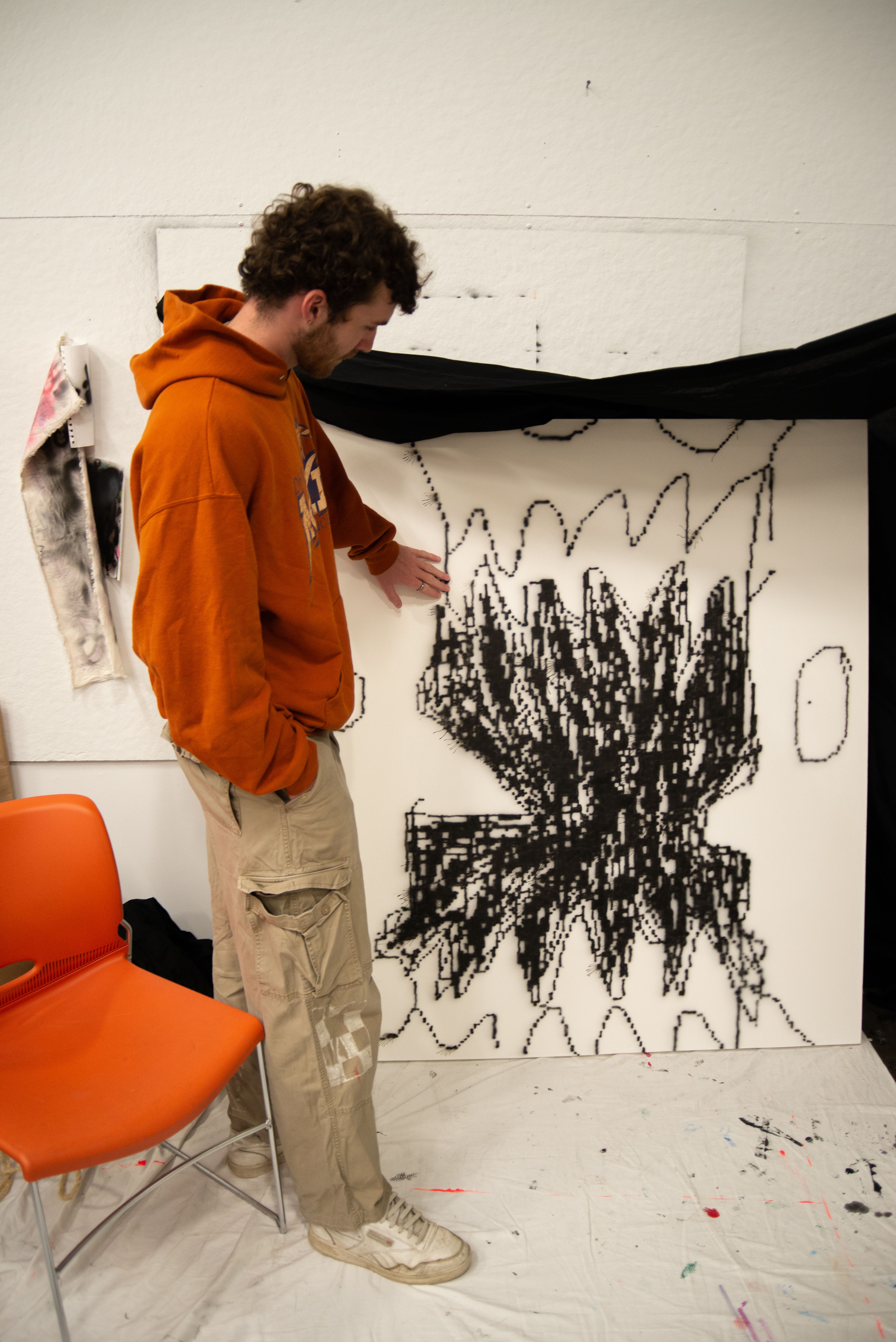 MFA student pointing towards an in-progress piece of pixelated scribbles.