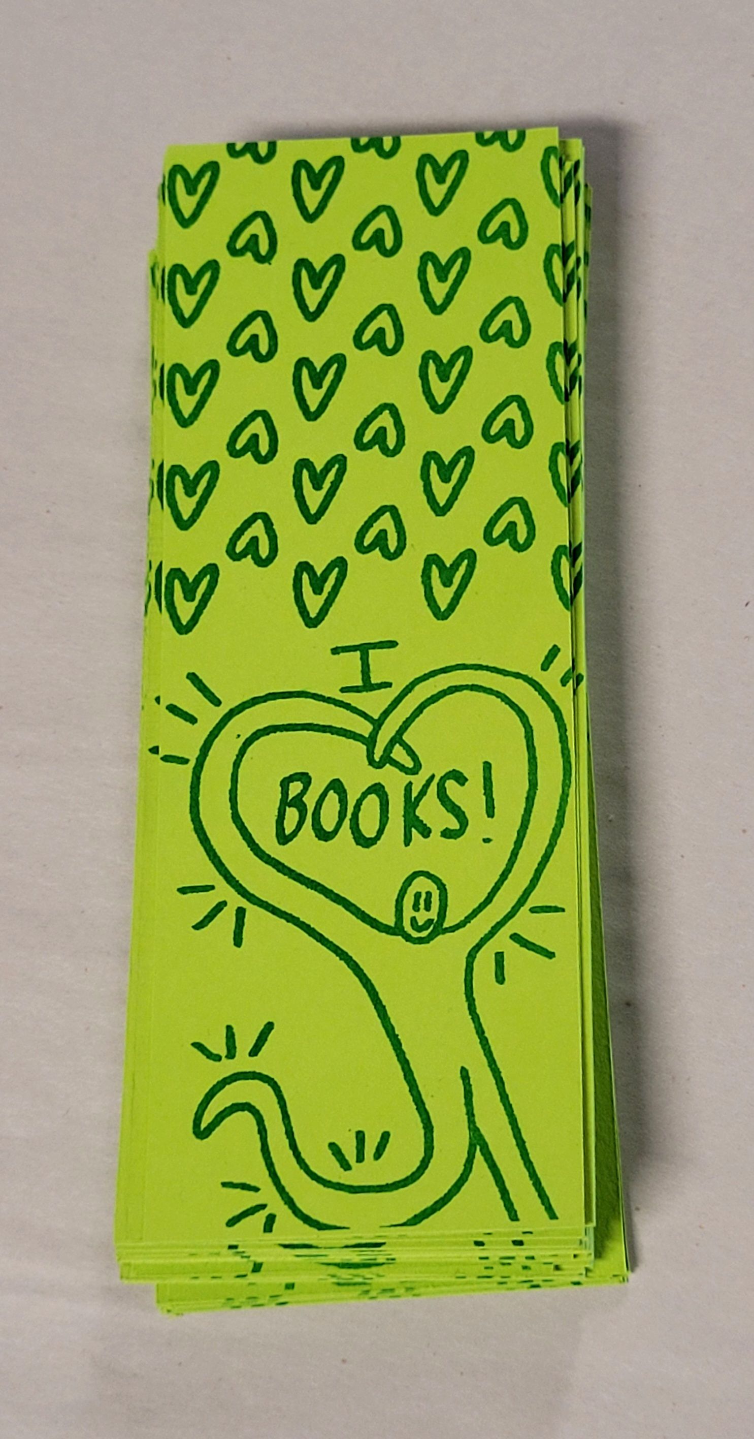 A green bookmark with a heart pattern and a figure saying "I heart books"