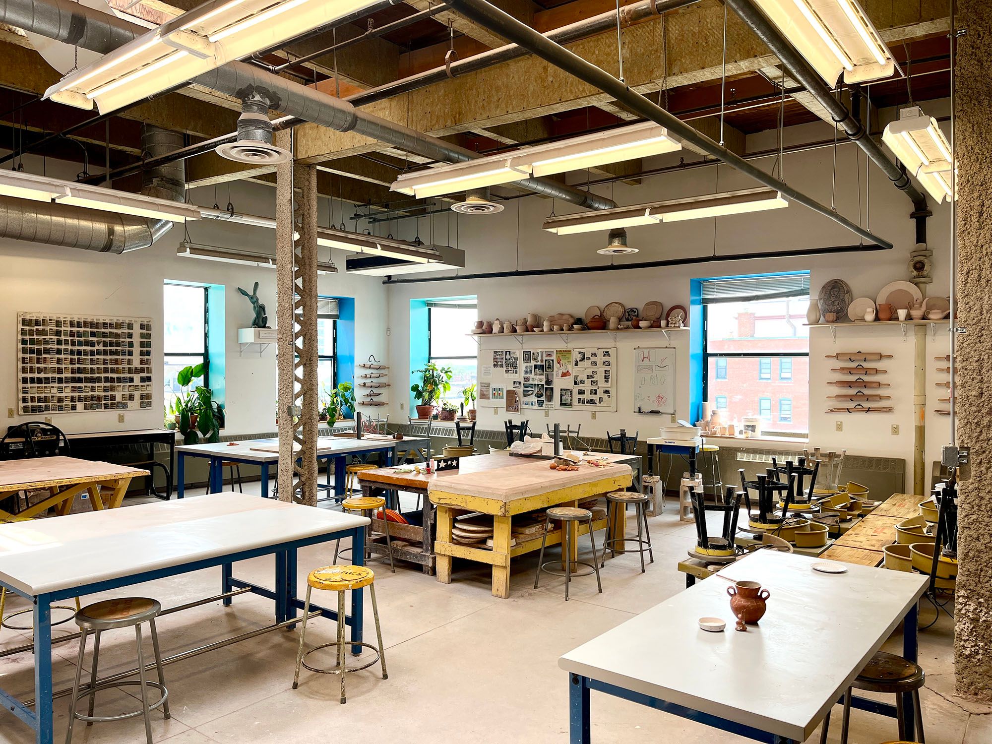 View of the ceramics classroom with several work tables and shelves crowded with ceramic objects.