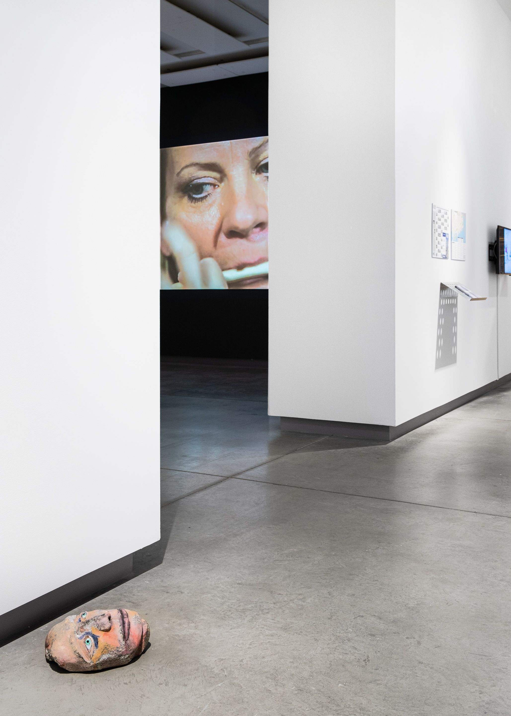 Installation view of a carved head on the floor and a projection of a face.